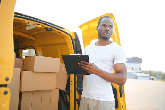 Sorridi l'uomo maschio africano del corriere di consegna postale davanti all'automobile che consegna il pacchetto