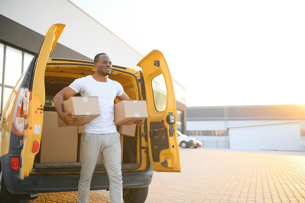 Sorridi l'uomo maschio africano del corriere di consegna postale davanti all'automobile che consegna il pacchetto