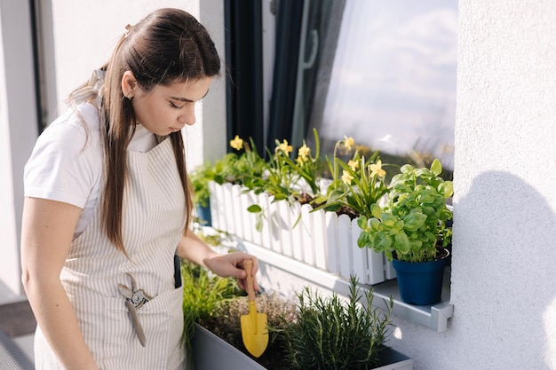 Sorrise giovane femmina creando giardino al balcone Donna che utilizza una piccola vanga per piantare A partire per l'atterraggio