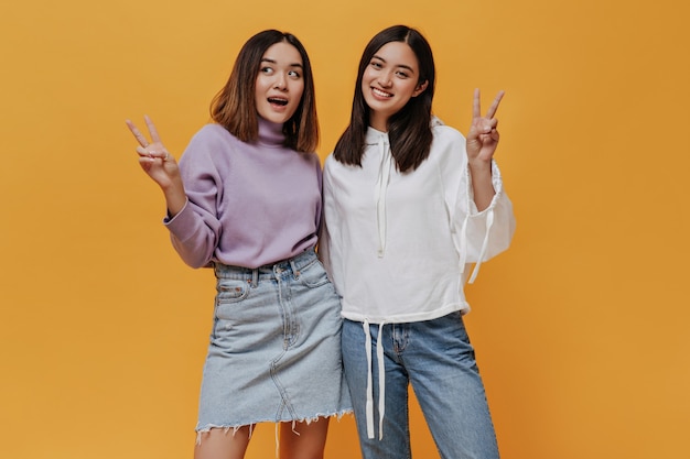 Sorrisi di donna sorpresa dai capelli corti in maglione viola e gonna. Affascinante ragazza in jeans e felpa con cappuccio posa isolata