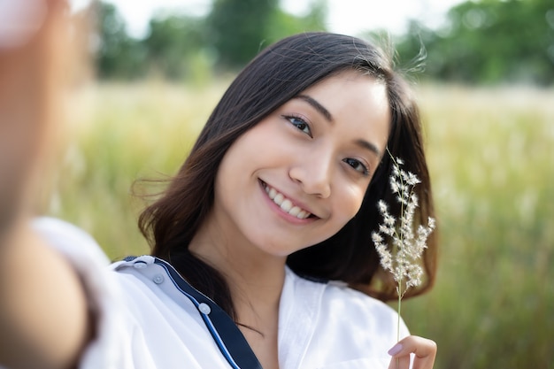 Sorrisi felici delle donne asiatiche che prendono le foto e Selfie su tempo di rilassamento al prato e all&#39;erba