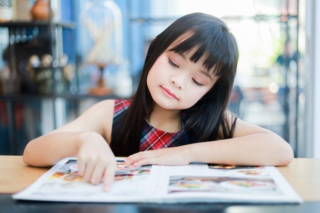 Sorriso asiatico del libro di lettura della bambina e fronte felice