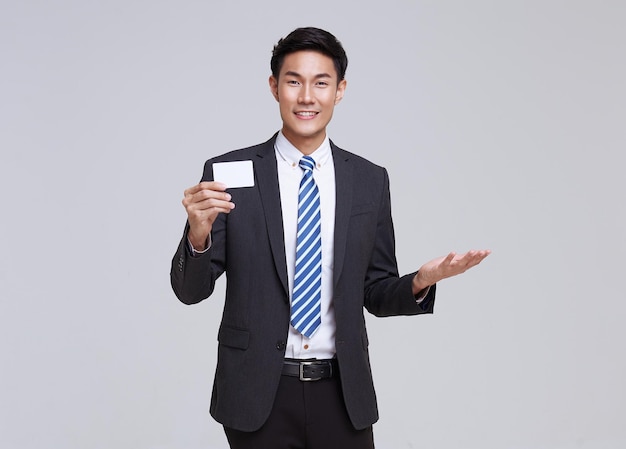 Sorriso asiatico dell'uomo d'affari in vestito convenzionale che mostra la carta di credito del modello sul colpo bianco dello studio del fondo