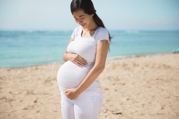 Sorriso asiatico della donna incinta mentre toccando la sua pancia