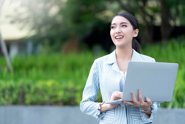 Sorriso attraente allegro asiatico femmina imprenditrice laptop connectin tecnologia di comunicazione giardino esterno posizione copysapce gratuito