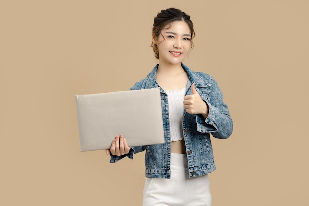 Sorriso bella donna asiatica che tiene tabellone per le affissioni bianco vuoto e pollice in alto su sfondo beige isolato