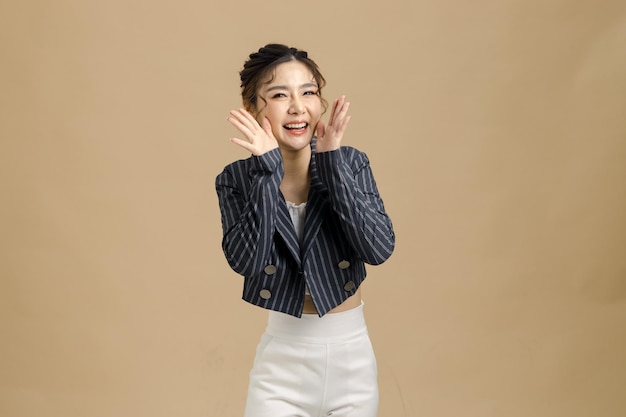 Sorriso bella donna d'affari asiatica bocca aperta alzando le mani urlando su sfondo beige isolato