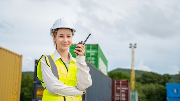 Sorriso del caposquadra della donna che usa il walkie-talkie davanti al carrello elevatore del carico nel magazzino Manager con il casco bianco Supervisore della sicurezza nel concetto di porto del terminal personalizzato del container import export