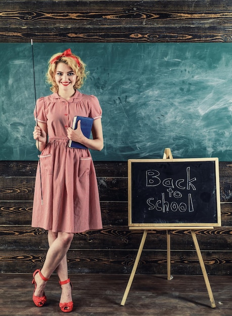 Sorriso dell'insegnante con libro e puntatore in classe. Insegnante felice torna a scuola su sfondo lavagna. Bella e geniale