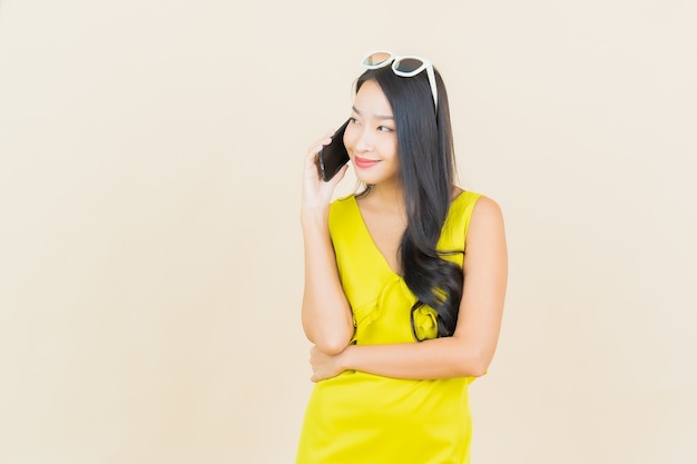 Sorriso della bella giovane donna asiatica del ritratto con il telefono cellulare astuto sulla parete di colore