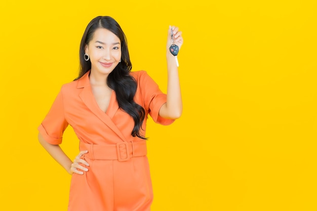 Sorriso della bella giovane donna asiatica del ritratto con la chiave dell'automobile su colore giallo