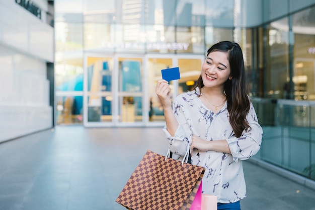 sorriso della donna con i sacchetti della spesa goda di utilizzare la carta di credito nel centro commerciale