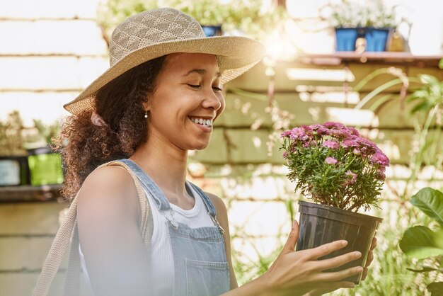 Sorriso della donna e pianta del vaso di fiori durante lo shopping al negozio di fiori per l'acquisto di piante da giardinaggio in un vivaio e negozio di giardinaggio Femmina nera o cliente felice con fiori in vendita in una serra