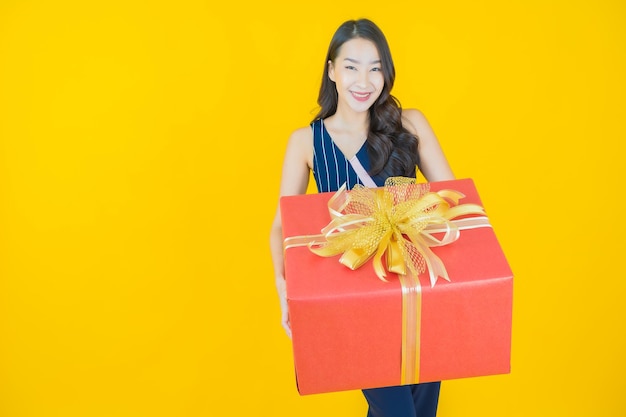 Sorriso di bella giovane donna asiatica del ritratto con il contenitore di regalo rosso acceso