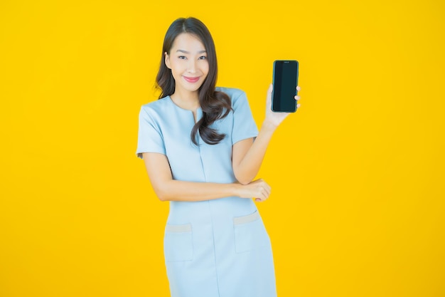 Sorriso di bella giovane donna asiatica del ritratto con il telefono cellulare astuto sul fondo di colore