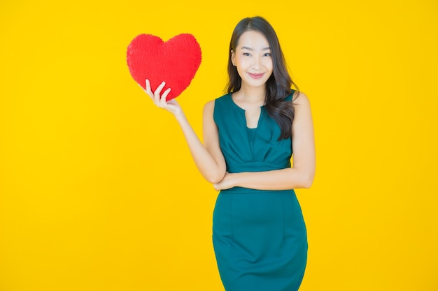 Sorriso di bella giovane donna asiatica del ritratto con la forma del cuscino del cuore su yellow