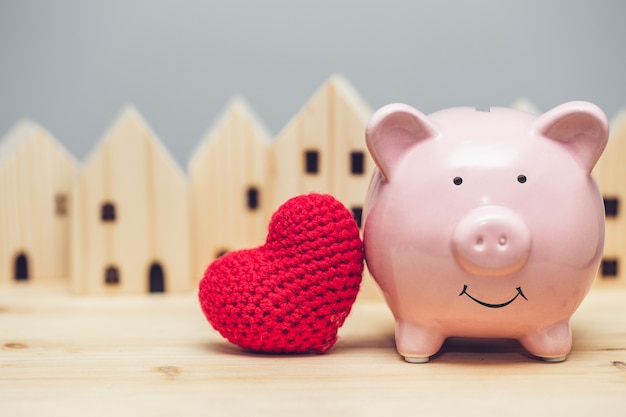 Sorriso di maiale carino con cuore rosso sullo sfondo del villaggio di casa per il concetto di casa sicura della comunità d'amore.