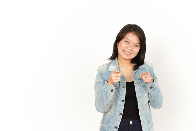 Sorriso e indicandoti di donna asiatica che indossa giacca di jeans e camicia nera isolata su bianco