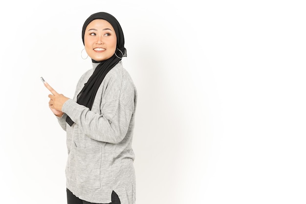 Sorriso e utilizzo di smartphone di bella donna asiatica che indossa l'hijab isolato su sfondo bianco