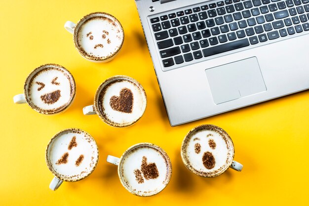 Sorriso emoji dipinto su tazze di cappuccino accanto al portatile