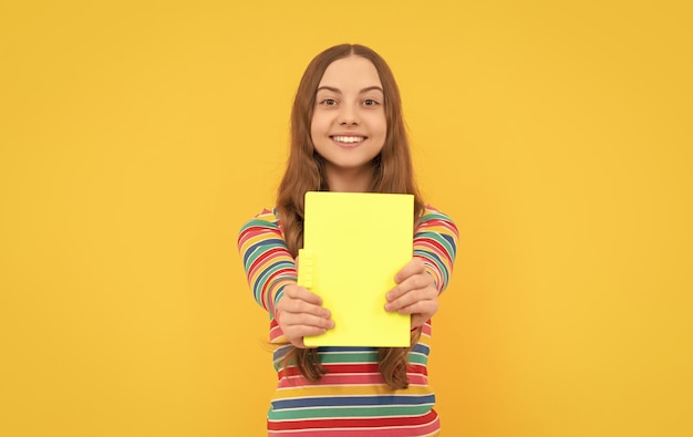 Sorriso felice del bambino che mostra il libro di scuola per la conoscenza del fondo giallo dello spazio della copia