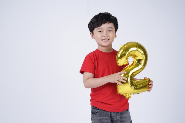 Sorriso felice del ragazzino asiatico con il numero della stagnola palloncino, isolato su sfondo bianco