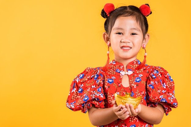 Sorriso felice della bambina cinese asiatica che porta il cheongsam rosso che tiene il lingotto d'oro