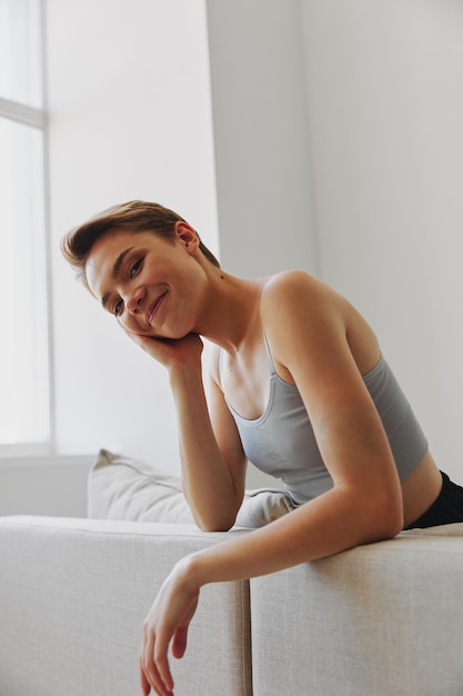 Sorriso felice della donna che si trova a casa sul divano che si rilassa durante un fine settimana a casa con un taglio di capelli corto capelli senza filtri su uno spazio libero della copia del fondo bianco