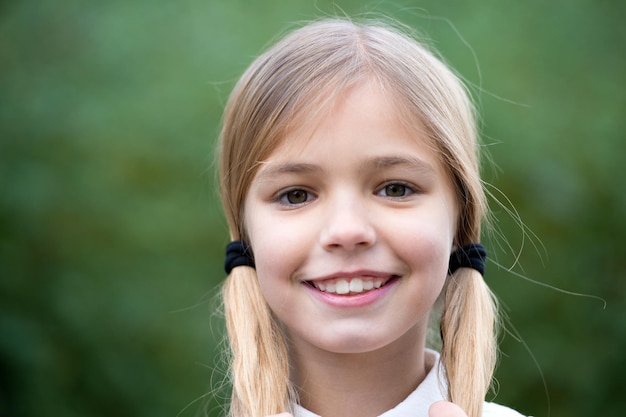 Sorriso felice della ragazza con le code di cavallo dei capelli biondi sull'ambiente naturale