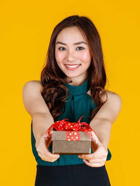 Sorriso felice faccia carina ragazza asiatica con i capelli scuri che tiene in mano un regalo e spinge avanti l'offerta con delizioso ed eccitato, girato in studio su sfondo giallo. Celebrare e concetto di festival.