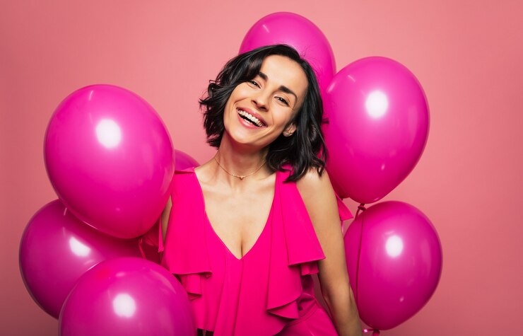 Foto sorriso hollywoodiano. foto ravvicinata di una giovane donna affascinante in un vestito rosa, che ride di gioia, circondata da palloncini rosa.