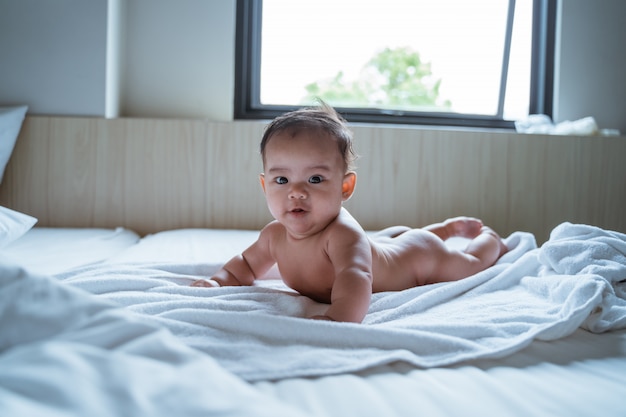 Sorriso nudo del bambino incline mentre trovandosi sul letto