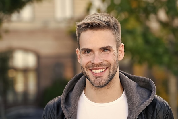 Sorriso perfetto Ritratto di ragazzo bello Capelli facciali e concetto di cura della pelle Viso bello Uomo bello viso con la barba lunga e capelli alla moda Uomo caucasico Sfondo urbano Uomo barbuto in stile casual