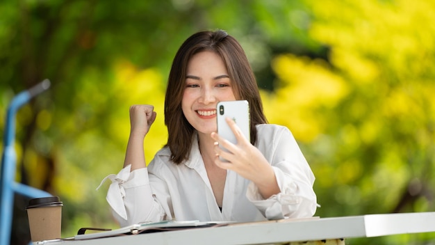 Sorriso premuroso Donna felice che videochiama online o si incontra online lavorando con uno smartphone in un parco