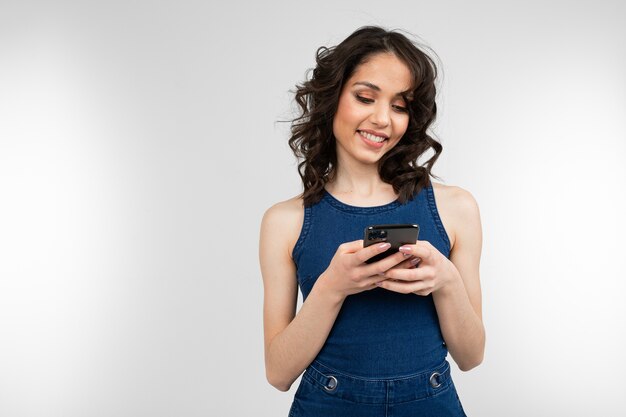 Sorriso ragazza in un vestito blu con uno smartphone in mano su uno sfondo grigio studio.