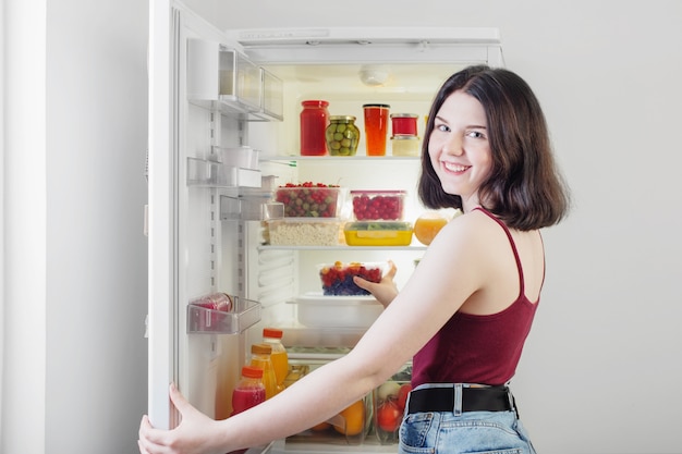 Sorriso ragazza vicino al frigorifero con cibo sano