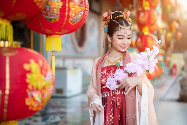 Sorriso ritratto Bambina asiatica carina che indossa costumi cinesi e tiene rami di fiori rosa per il festival del capodanno cinese celebra la cultura cinese al santuario cinese Luoghi pubblici in Thailandia