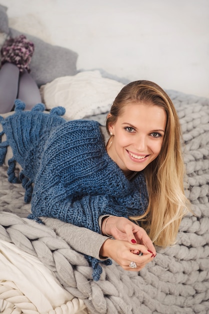 Sorriso sincero. Splendida giovane donna che guarda la macchina fotografica e sorride mentre è sdraiata sul letto a casa in inverno