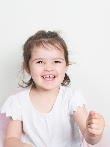 Sorriso sveglio allegro della ragazza del bambino del bambino felice in vestiti e fondo bianchi