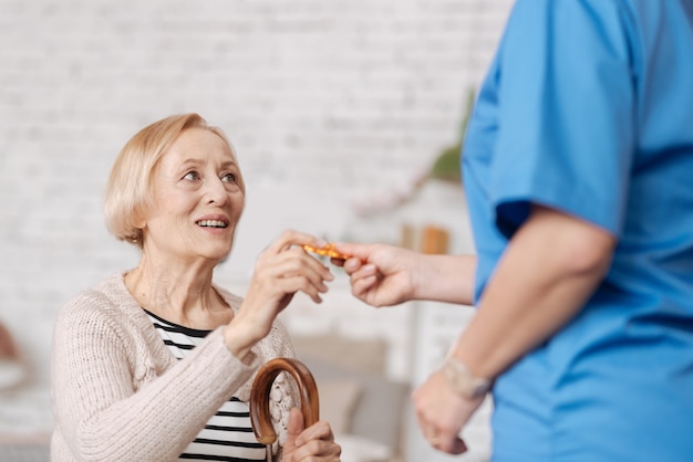 Sostenere la salute. Notevole donna diligente competente che prescrive alcune vitamine della vecchia signora dopo averle fatto visita a casa e aver eseguito un esame