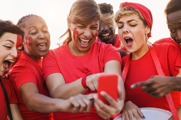 Sostenitori sportivi multirazziali che guardano una partita di calcio sul cellulare Focus principale sul volto della donna centrale