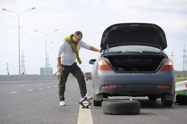 Sostituzione della ruota di un'auto sulla strada. Un uomo che fa il lavoro sui pneumatici in disparte.