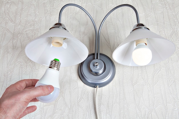 Sostituzione delle lampadine elettriche nella lampada da parete per uso domestico, lampadina a LED in mano umana, primo piano.