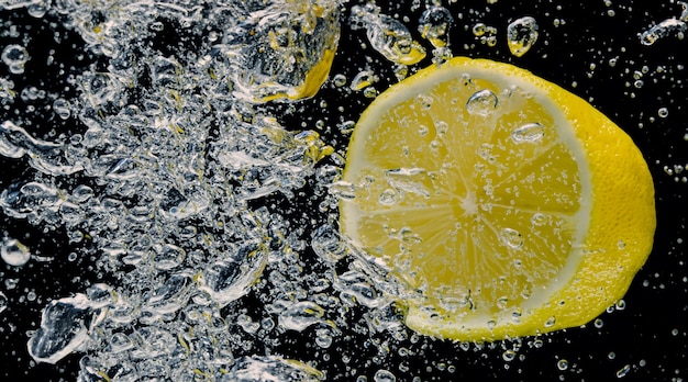 Sott'acqua di limonata zuccherata appena spremuta che fetta di limone crudo che cade in acqua gassata su sfondo blu scuro o nero Primo piano della limonata o della bevanda rinfrescante fredda del cocktail Highball al limone