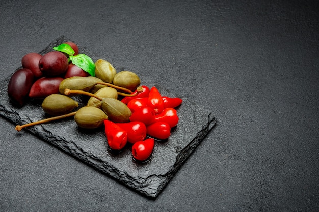 Sottaceti misti su tavola di pietra. Olive, Capperi e Peperoni