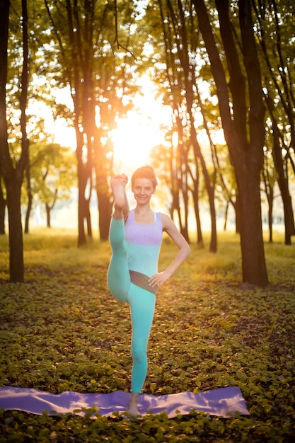 Sottile ragazza bruna gioca sport ed esegue pose yoga nella sosta di autunno su un tramonto