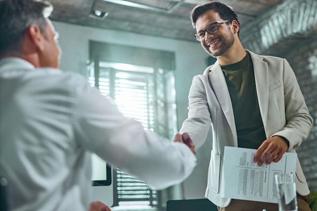 Sotto la vista del candidato felice che saluta un uomo d'affari durante un colloquio di lavoro in ufficio