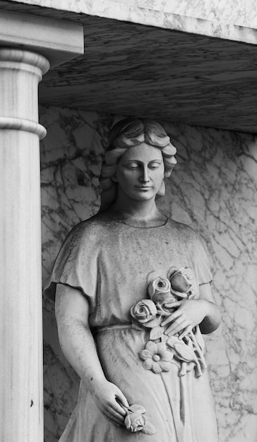 Sotto un pilastro c'è una statua di una donna con dei fiori in mano.
