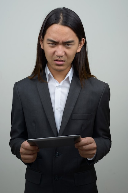 Sottolineato giovane imprenditore asiatico con i capelli lunghi che sembra arrabbiato durante l'utilizzo di tavoletta digitale