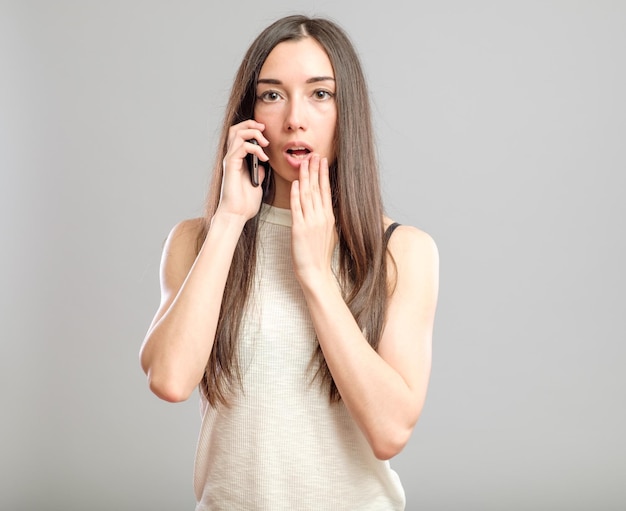 Sottolineato stanco e preoccupato giovane donna che parla al telefono isolato su sfondo grigio